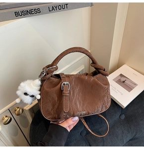 Detailed close-up of brown textured cloud bag with metal logo and plush doll pendant