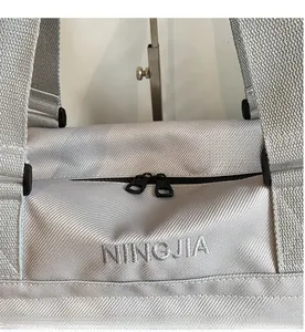 Dettaglio delle doppie cerniere nere e ricamo su una borsa da viaggio in tessuto grigio