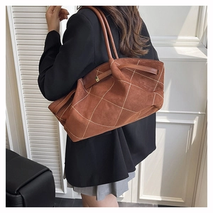 Detail of tan suede tote bag with white diamond stitching shown on a model shoulder
