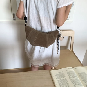 Détail d'un sac croissant en daim marron avec bandoulière à nœud et ours en peluche