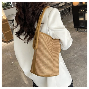 Detail of woven straw bucket bag with brown leather trim and handle for women