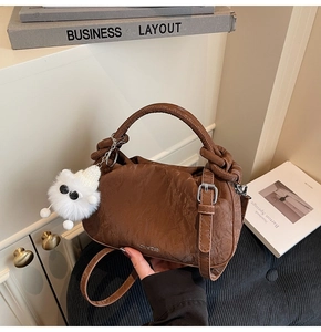 Detail of dark brown pleated cloud bag with white plush monster charm and slim strap