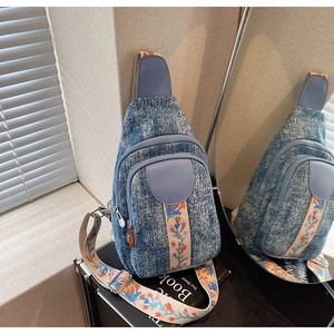 Close-up of blue denim crossbody bag with embroidered floral strap and zipper details