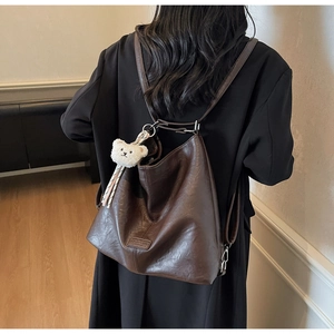 Detail of dark brown vintage PU leather backpack with a plush bear charm on a model