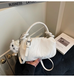 Detail of white textured cloud bag with decorative knot handle and plush monster charm