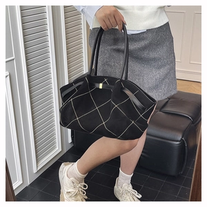 Detail of black suede tote bag featuring white quilted diamond stitching and gold hardware