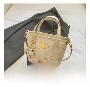 Detail der cremefarbenen Eimertasche mit Katzenprint und goldener Metall-Logo-Plakette