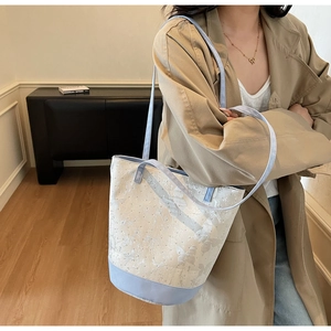 Close-up of canvas bucket bag with butterfly pattern and light blue trim on a model