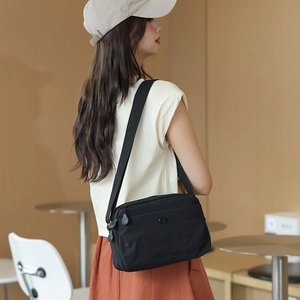 Detail of black nylon crossbody bag with wide strap worn in a cozy cafe setting