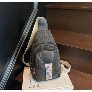 Detail of grey denim sling bag showing colorful bohemian strap and textured fabric