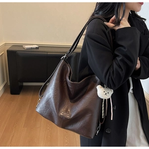 Detail of dark brown tote bag with textured synthetic leather and plush bear charm