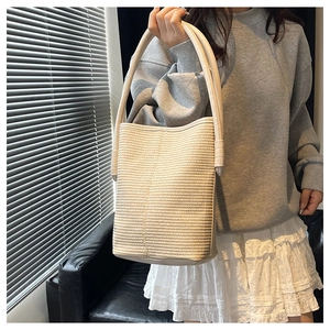 Close-up of a cream woven bucket bag with detailed straw texture and a wide leather strap