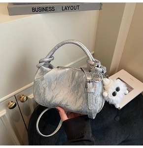 Silver metallic dumpling bag with a white plush monster keychain on a book background