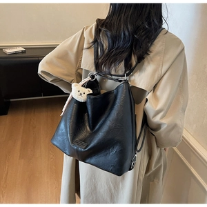Detailed macro view of black faux leather texture and plush bear charm on the tote bag