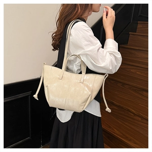 Detail view of beige patent leather tote bag with side drawstring and glossy finish texture