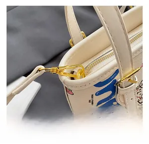 Détail du sac graffiti crème montrant les crochets dorés et la fermeture éclair fluide
