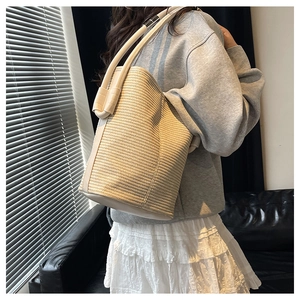 Detail of woven straw bucket bag with cream faux leather handle and stylish stitching