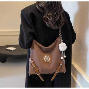 Dettaglio di una borsa hobo retrò marrone con logo M e ciondolo a nuvola su cappotto