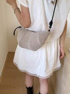 Sac bandoulière minimaliste en daim beige porté par un mannequin femme en robe