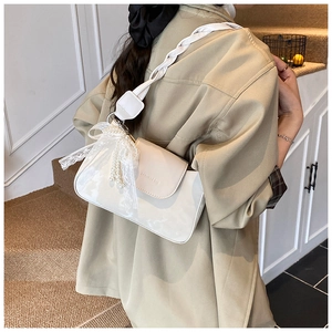 Detail of cream white underarm bag with woven strap, lace bow and pearl charm