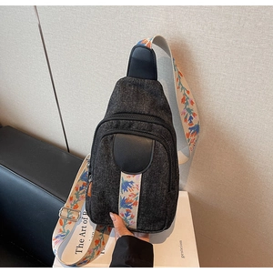 Detail of black denim crossbody bag featuring a wide floral embroidered shoulder strap