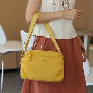 Detail of a bright yellow nylon crossbody bag featuring double zippers and a metal logo