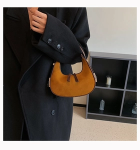 Detail of a ginger suede half-moon underarm bag with brown leather trim and metal zipper