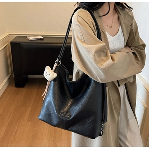 Detail of black leather hobo bag with a white plush bear charm and brand logo