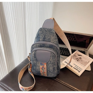 Detail of blue denim crossbody bag featuring floral embroidered beige strap and zippers