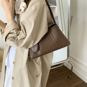 Dettaglio della texture in pelle intrecciata marrone e fibbia della borsa a spalla