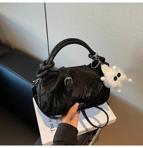 Detail of black cloud bag featuring pleated texture, knotted handle, and plush charm