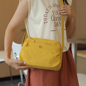 Detailed view of yellow nylon crossbody bag featuring wide strap and stylish metal logo