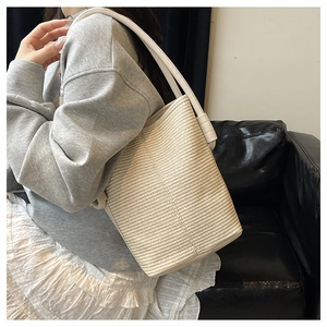Detail view of woven beige bucket bag with matching leather strap and textured fabric