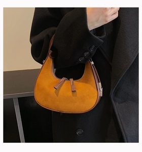 Detail of yellow suede crescent bag with dark brown leather piping on black wool coat