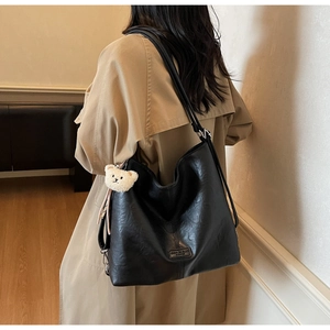 Detail of black tote bag featuring leather texture and a cute white teddy bear charm