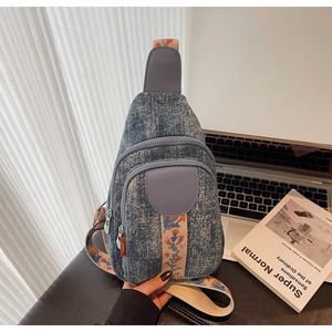 Detail of blue denim crossbody bag featuring a colorful floral embroidered shoulder strap