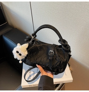 Detail of black pleated leather cloud bag with white plush charm and buckled strap