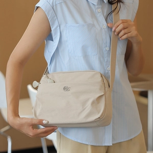 Detail of beige nylon crossbody bag with multi-layer zippers and metallic logo