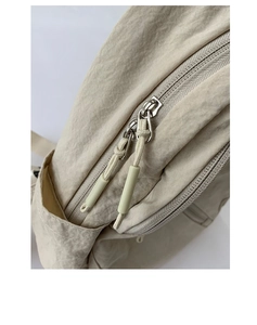 Detailed macro view of cream nylon fabric texture and metal zipper pull on a casual backpack