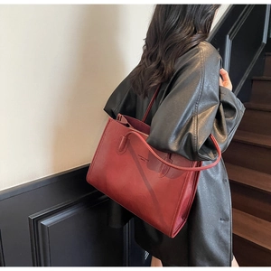 Detail view of a large burgundy tote bag in matte leather worn by a model in a black jacket