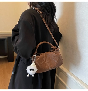 Detail of brown pleated cloud bag with soft texture and cute white plush pendant