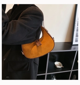 Detail view of mustard yellow suede crescent underarm bag worn by model in a modern setting