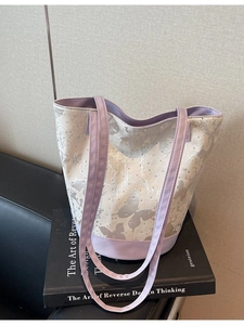 Canvas bucket bag with butterfly print, purple trim and studs on a leather sofa