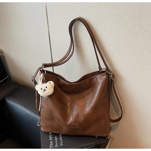 Detail of vintage brown leather tote bag showing smooth texture and plush bear charm