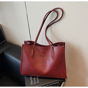 Detail showing vintage dark red leather texture and embossed logo on the tote bag