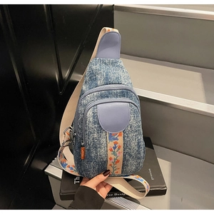 Detail of blue washed denim crossbody bag with floral embroidery and dual zippers