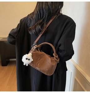 Brown leather crossbody cloud bag with plush pendant shown from behind on a model