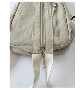 Detail of beige nylon chest bag showing multi-pocket zipper and durable webbing strap