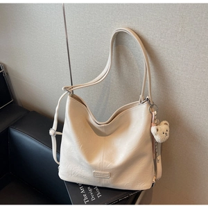Detail of off-white tote bag with grainy faux leather texture and plush bear pendant