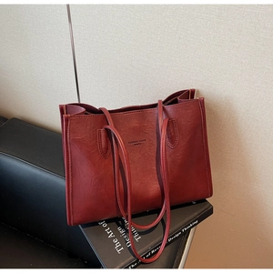 Detail of dark red tote bag featuring Fashion Trend lettering on black sofa setting